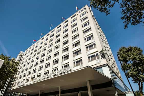 Lejlighedsbygning med synlige vinduer og flag på taget. (AI-genereret tekst)