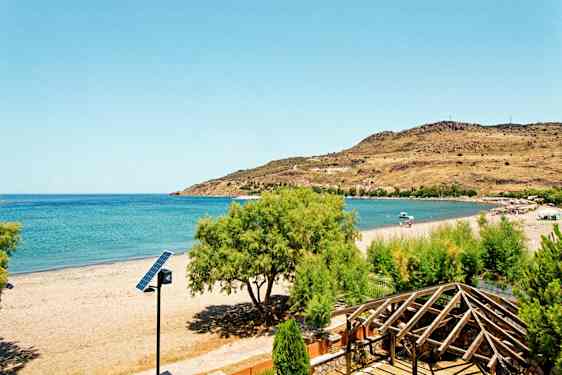 En strand med klart blåt hav, omgivende grønt og en trækonstruktion i forgrunden. (AI-genereret tekst)