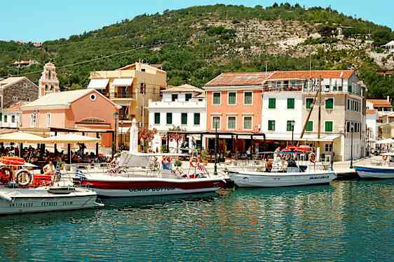 En havn med flere både foran farverige bygninger og omgivet af bakker. (AI-genereret tekst)