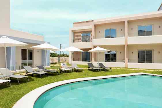 Poolområde med liggestole og parasoller foran lyse bygninger. (AI-genereret tekst)