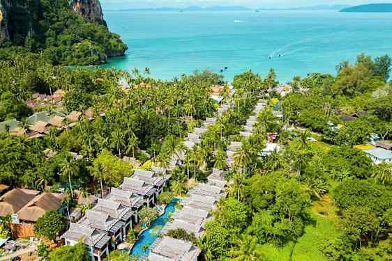 Luftfoto af et tropisk område med palmer, bygninger og en pool, med havet i baggrunden. (AI-genereret tekst)