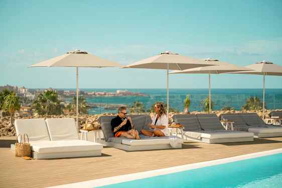 Liggestole og parasoller ved en pool med udsigt over havet. (AI-genereret tekst)