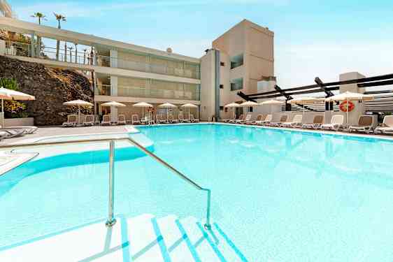 En pool med klart blåt vand omgivet af liggestole og parasoller. (AI-genereret tekst)