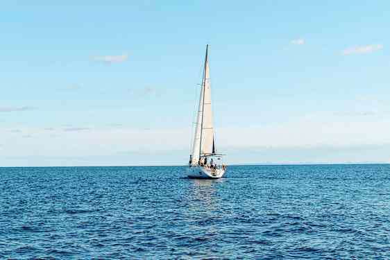 En sejlbåd sejler på et åbent hav under en klar himmel. (AI-genereret tekst)