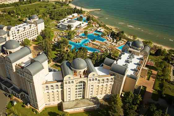 Luftfoto af et hotelkompleks med pools og strand. (AI-genereret tekst)