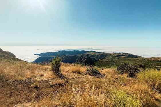 Solrig bjergudsigt med skyet panorama og tør vegetation. (AI-genereret tekst)