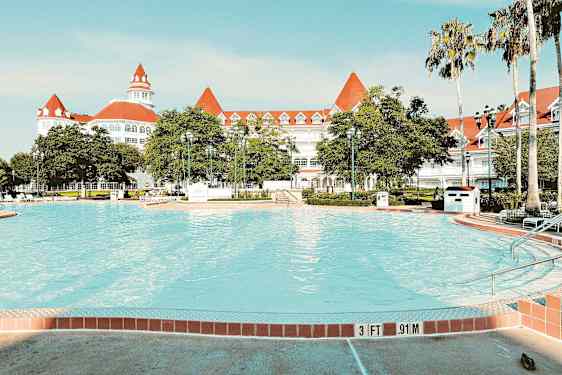 Billede af en swimmingpool med et elegant hvidt hotel med røde tage i baggrunden. (AI-genereret tekst)