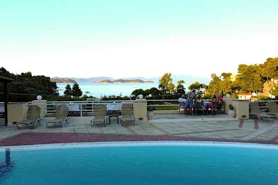 Udsigt fra en poolterrasse med liggestole, med hav og øer i baggrunden. (AI-genereret tekst)
