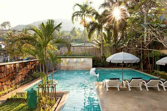 En solbeskinnet pool omgivet af palmer og liggestole. (AI-genereret tekst)