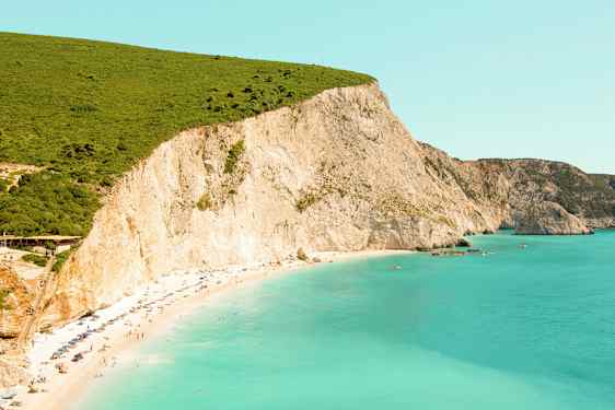 En strand med turkis vand og store klipper i baggrunden. (AI-genereret tekst)