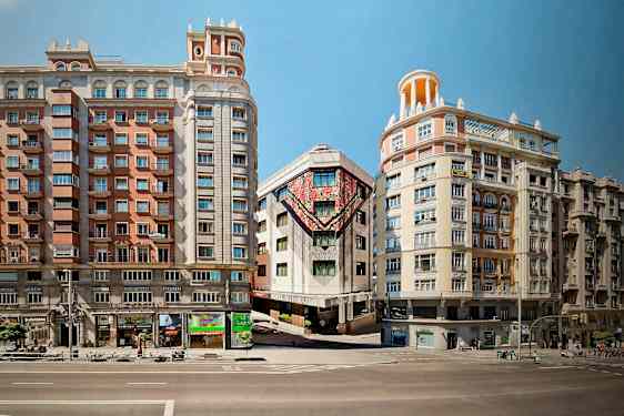 Tre bygninger ligger langs en gade, hvor midtbygningen har farverige kunstværker på facaden. (AI-genereret tekst)