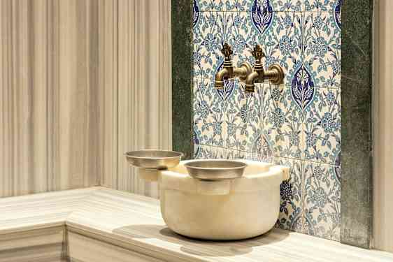 En vandhane med orientalske fliser i baggrunden og en marmorskål nedenunder. (AI-genereret tekst)