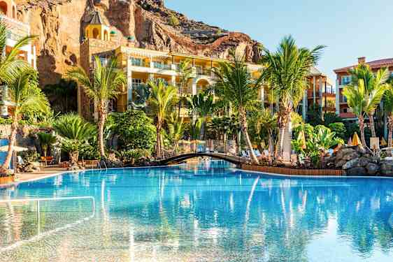 En pool omgivet af palmer og ferieboliger. (AI-genereret tekst)