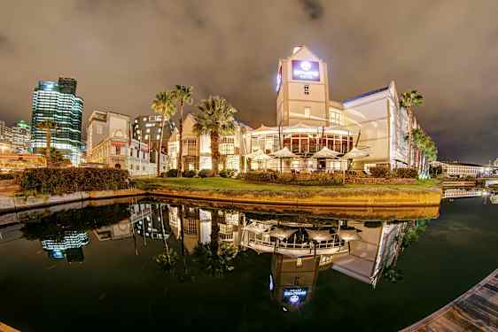 Hotel og bygninger ved en kanal om aftenen med spejlreflekser i vandet. (AI-genereret tekst)