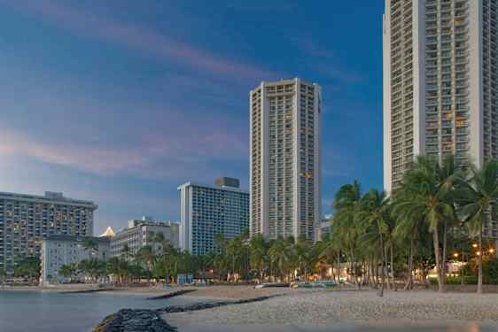 Høje bygninger ved en strand med palmer i skumringen. (AI-genereret tekst)