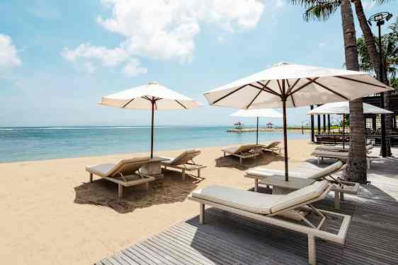 En strand med liggestole og parasoller ved et klart blåt hav. (AI-genereret tekst)