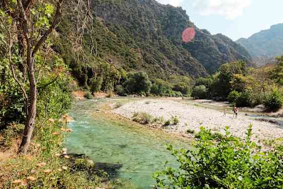 En flod med klart vand, der løber gennem et frodigt landskab med bjerge i baggrunden. (AI-genereret tekst)