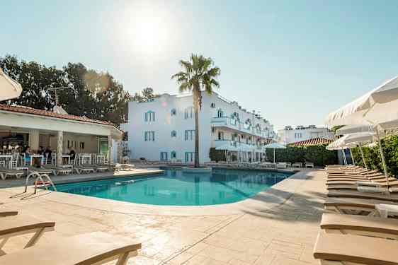 Billede af en pool med liggestole og parasoller; i baggrunden ses en hvid bygning og et åbent reservationsområde. (AI-genereret tekst)