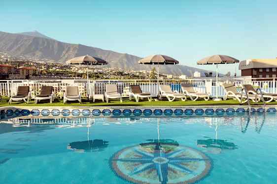 Poolområde med liggestole og parasoller med udsigt over bjerge og bygninger. (AI-genereret tekst)