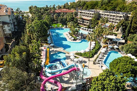 Udsigt over et resort med flere pools og vandrutsjebaner, omgivet af grønne områder. (AI-genereret tekst)