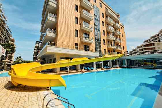 En bygning med altaner ved siden af en pool med en gul vandrutsjebane. (AI-genereret tekst)