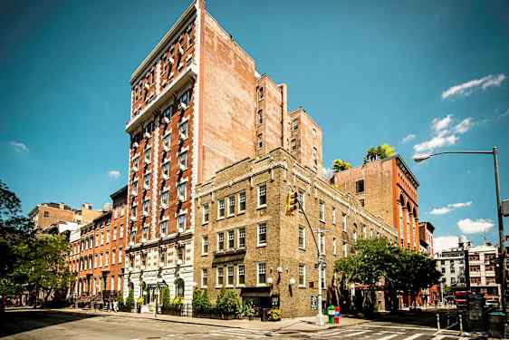 Flere murstensbygninger ved et gadehjørne under en klar blå himmel. (AI-genereret tekst)