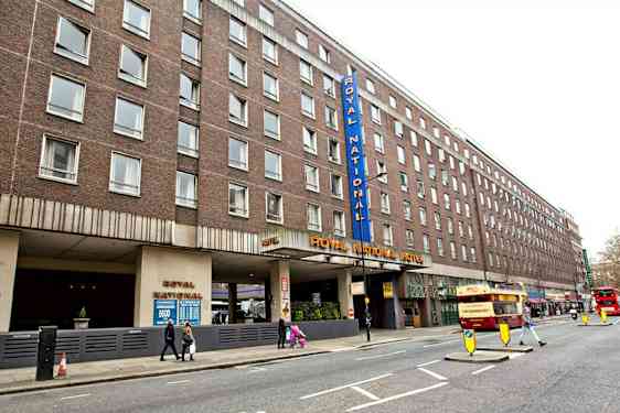 Billede af Royal National Hotel fra gaden med flere busser og fodgængere. (AI-genereret tekst)