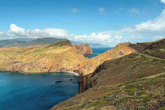 Et kystlandskab med høje klipper, grøn vegetation og havet, der breder sig i baggrunden under en blå himmel. (AI-genereret tekst)
