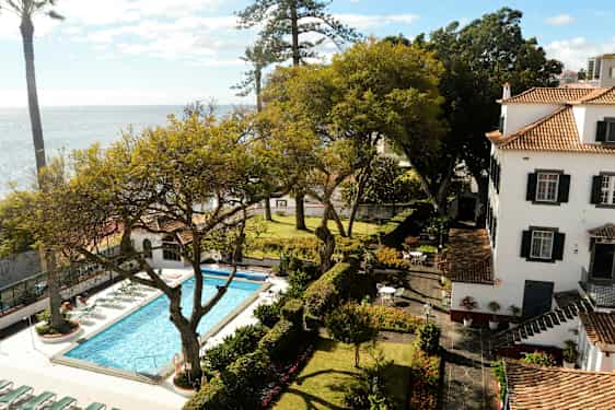 Et billede af en have med swimmingpool, omgivet af træer og en bygning i baggrunden. (AI-genereret tekst)