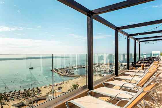 Liggestole opstillet foran glasværn med udsigt over strand og havn. (AI-genereret tekst)