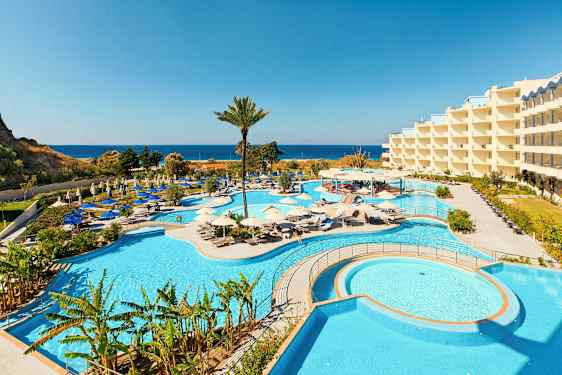 Billede af et hotelområde med store swimmingpools og omgivende liggestole samt havudsigt i baggrunden. (AI-genereret tekst)