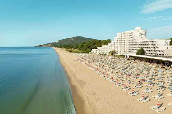 En lang sandstrand med liggestole og parasoller, samt et hotel og grønne bakker i baggrunden. (AI-genereret tekst)