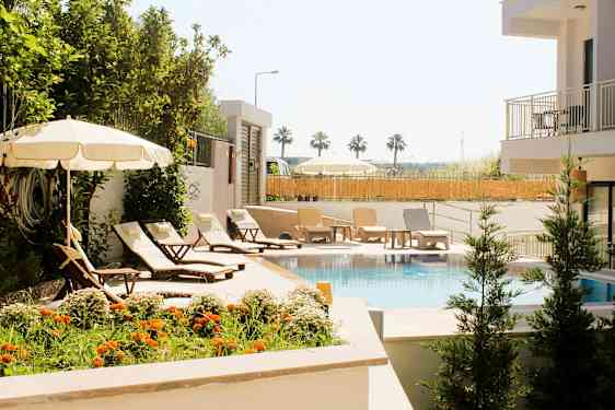 En pool omgivet af liggestole, parasoller og grønne omgivelser. (AI-genereret tekst)