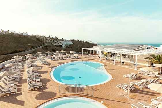 Poolområde med liggestole og parasoller på en terrasse med havudsigt. (AI-genereret tekst)