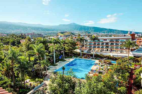 En pool omgivet af planter og bygninger med et bjerg i baggrunden. (AI-genereret tekst)