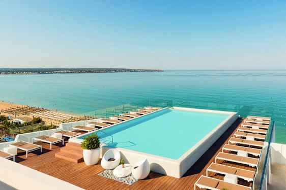 En tagpool med liggestole ved kanten og udsigt over en strand og hav. (AI-genereret tekst)