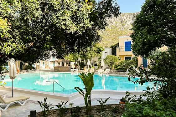 Billedet viser en pool omgivet af træer og liggestole. (AI-genereret tekst)