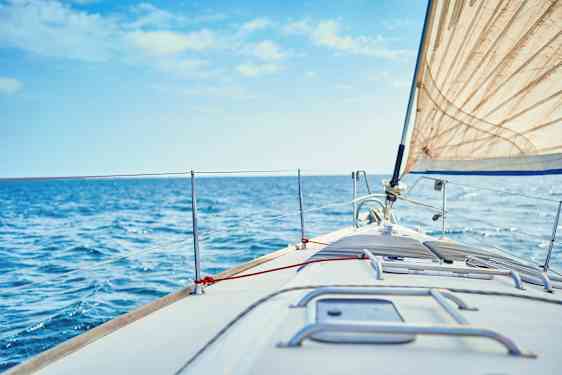 Nærbillede af fordækket på en sejlbåd, med et hvidt sejl og blåt hav i baggrunden. (AI-genereret tekst)