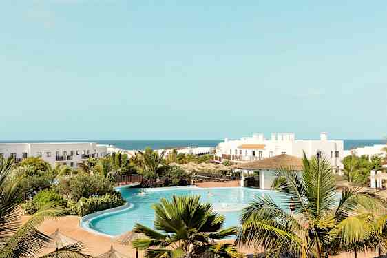 Hotelområde med pool, grønne omgivelser og havet i baggrunden. (AI-genereret tekst)