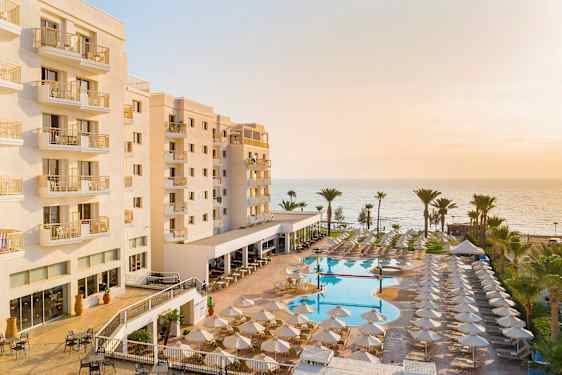 Hotel med altaner, poolområde og hav i baggrunden. (AI-genereret tekst)