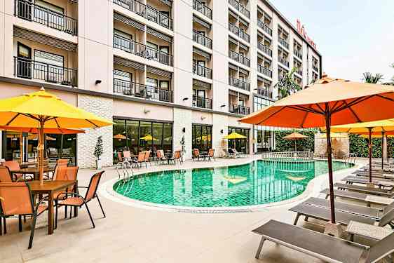 En hotelpool omgivet af liggestole og parasoller, med bygningen i baggrunden. (AI-genereret tekst)