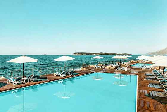 En swimmingpool ved havet, omgivet af solsenge og parasoller. (AI-genereret tekst)