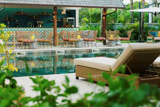 Billede af et poolområde med liggestole og en bar i baggrunden. (AI-genereret tekst)