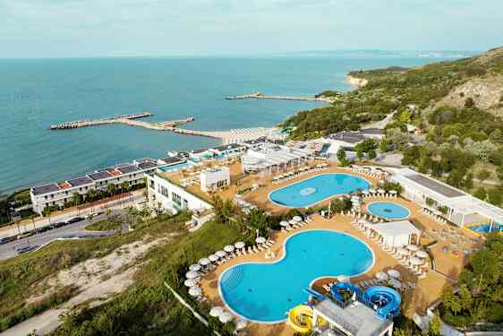 Billede af en ferieresort ved havet med pools, liggestole og frodige omgivelser. (AI-genereret tekst)
