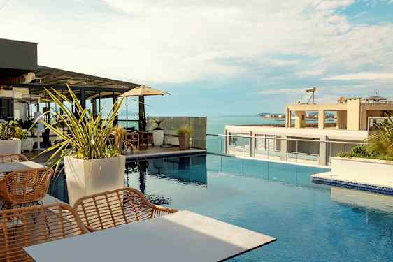 En tagterrasse med udsigt over havet, møbleret med borde, stole og parasoller ved en swimmingpool. (AI-genereret tekst)