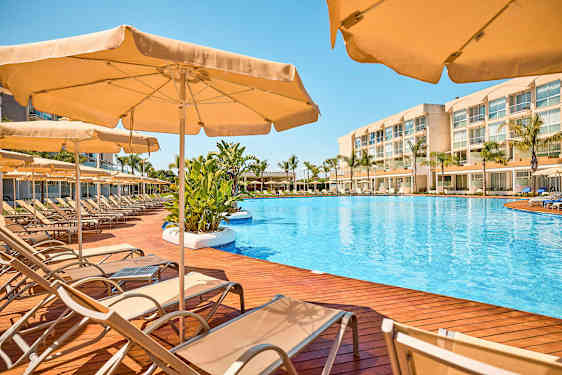 Poolområde med liggestole og parasoller på en træterrasse. (AI-genereret tekst)