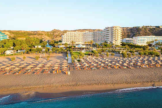 Strand med parasoller og liggestole, hotel og grøntområder i baggrunden. (AI-genereret tekst)