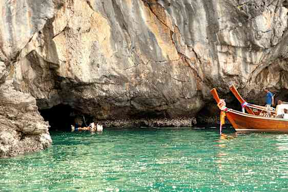 Personer svømmer i vandet ved en klippe, og to træfartøjer flyder tæt på. (AI-genereret tekst)