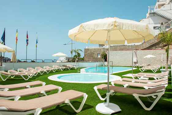 Udendørs poolområde med liggestole og parasoller, omgivet af grøn græsplæne. (AI-genereret tekst)