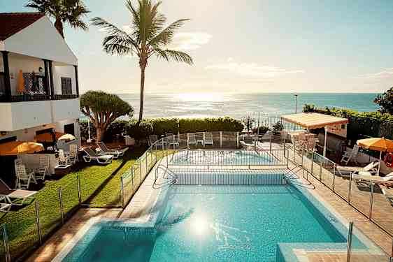 En udendørs pool med liggestole og parasoller ved siden af, med havet i baggrunden. (AI-genereret tekst)